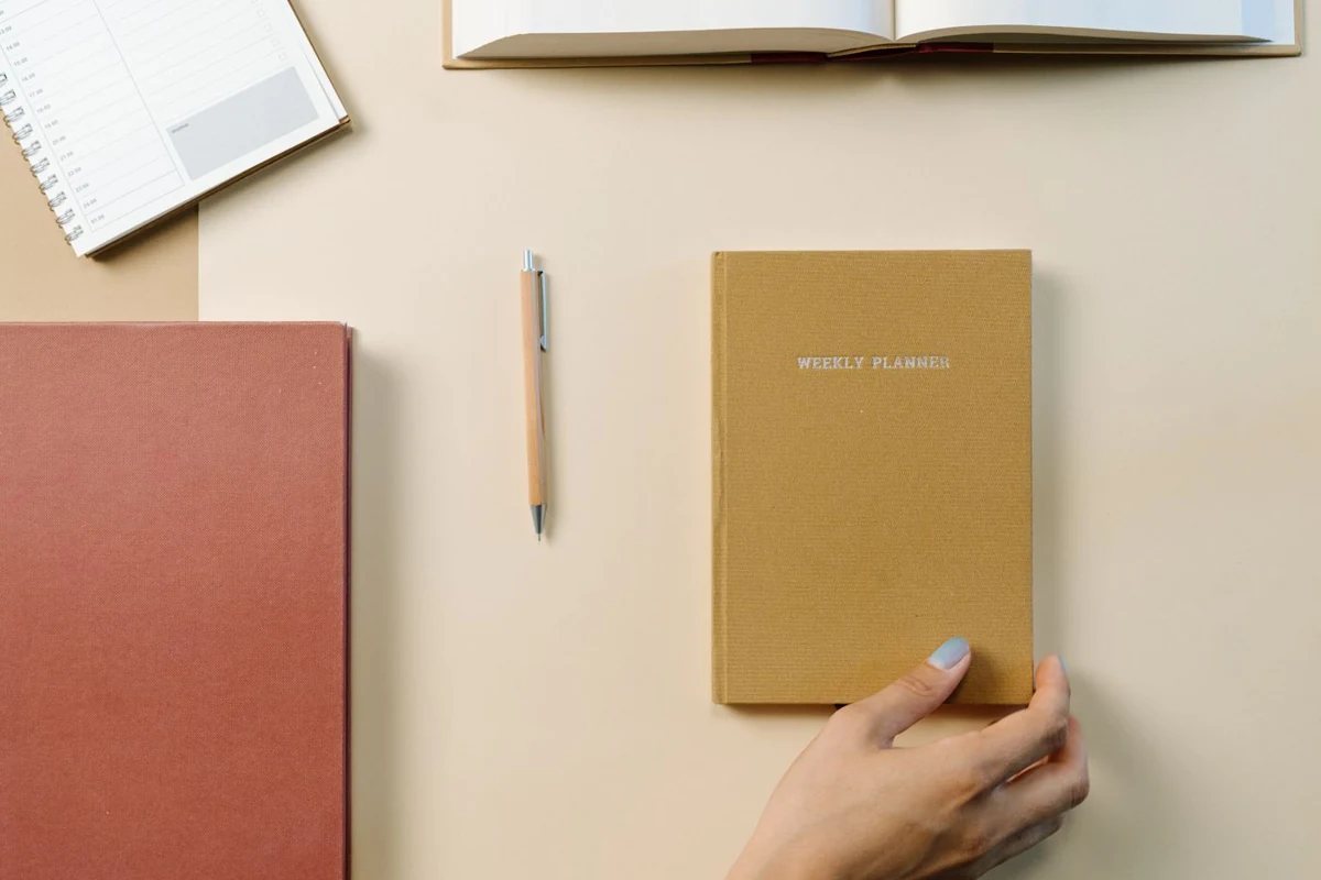 Notebook, pen and weekly planner on a desk.